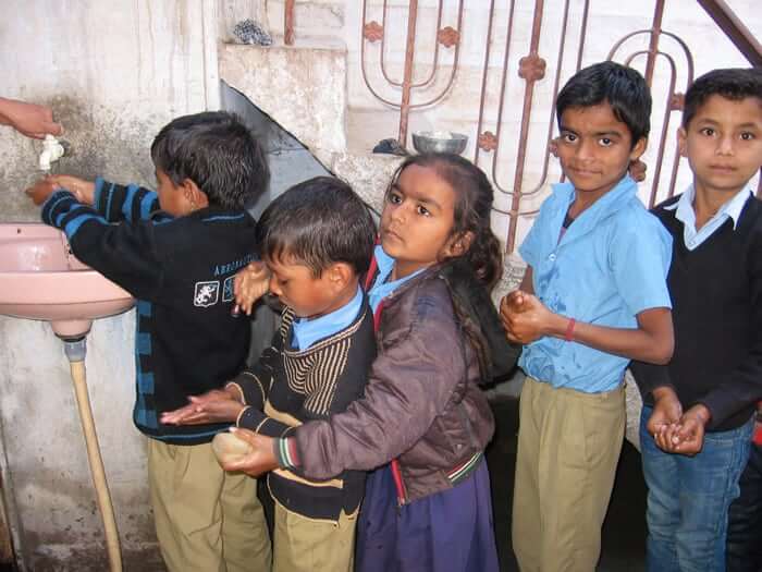 Children queue to wash hands before a meal.